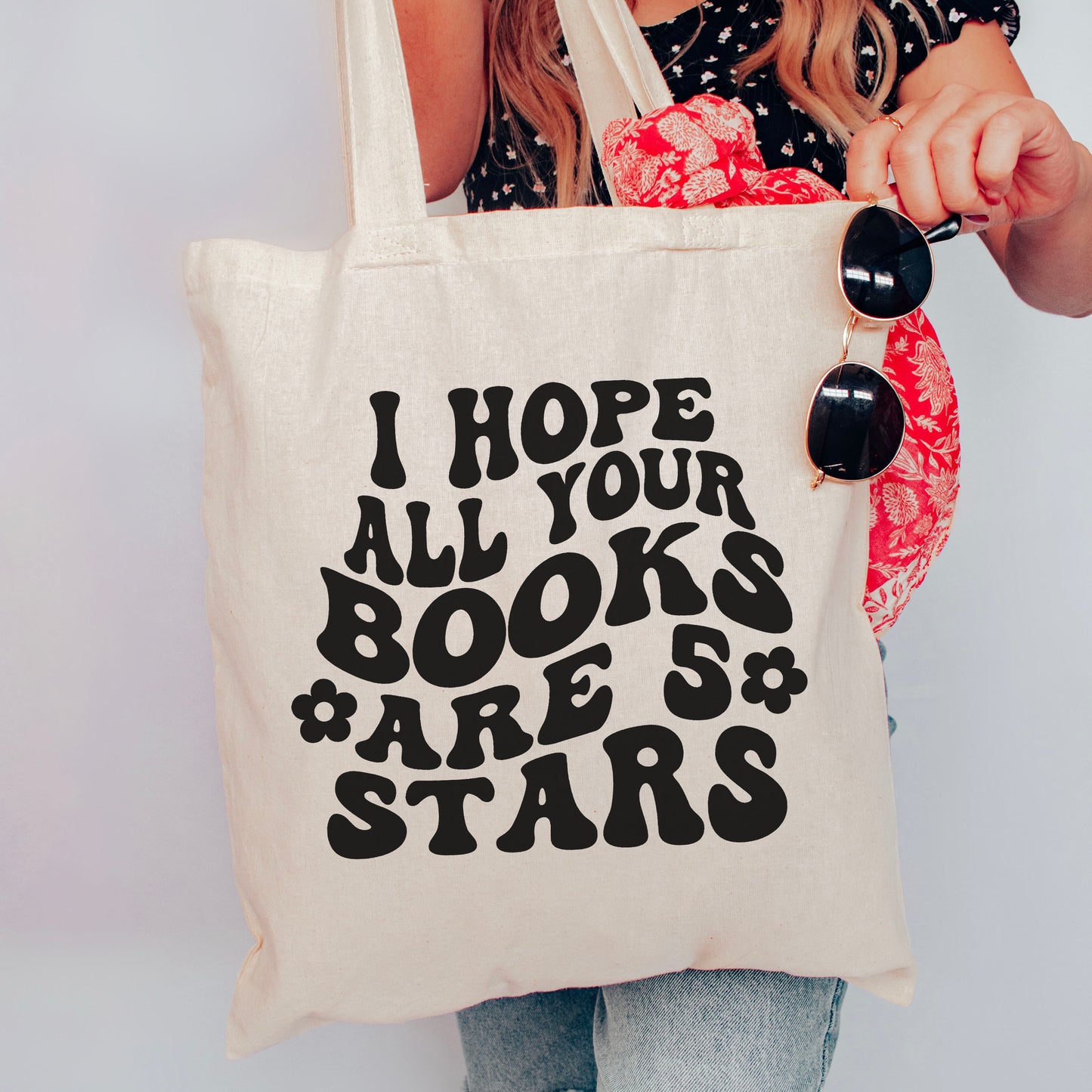 A natural canvas tote bag featuring a bold, retro-style design that reads "I Hope All Your Books Are 5 Stars." Held by a stylish reader accessorized with sunglasses and a floral scarf, this bookish tote is perfect for carrying books, everyday essentials, or bookstore hauls. A must-have for book lovers who adore aesthetic and literary-inspired accessories.